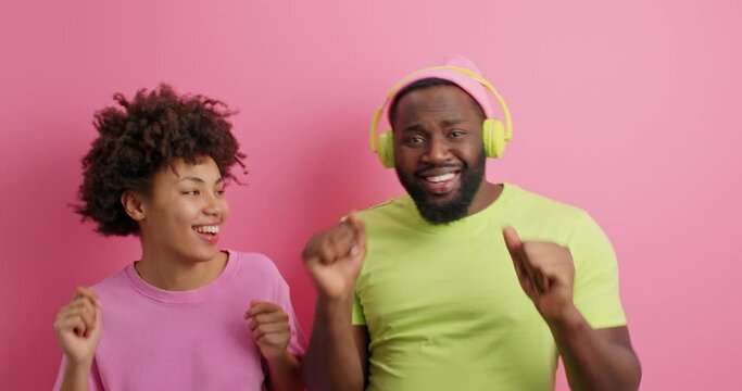 Positive enrgetic dark skinned woman and man dance carefree to favorite music have fun on disco party catch every bit of melody use stereo headphones dressed casually spend free time together