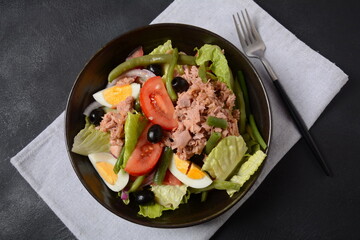 Salad Nicoise. French cuisine. Healthy salad of tuna, green beans, tomatoes, eggs, potatoes, black olives close-up in a bowl on the table.
