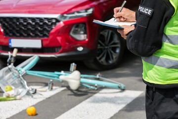 Policeman writes a ticket standing in front of a red car that hit a cyclist on a pedestrian lane