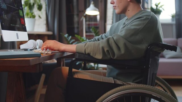 Midsection shot of young paraplegic woman on wheelchair using computer at desk while working remotely from home
