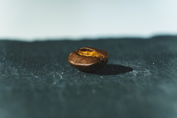 eine einzelne Kaffee Bohne auf einem Schiefer Stein Untergrund vor einem weichen Bokeh Hintergrund in stimmungsvollen Farben