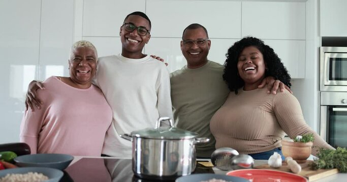 Happy latin family looking in camera and smiling - Parents and adult children having fun cooking together inside kitchen at home