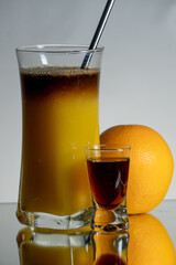 Brown, herbal layer drink with orange juice and straith metal straw. Single liqueur shot and fruit on the side. Reflection on the bottom and gradient background