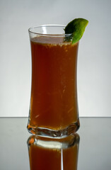 Brown herbal alcohol drink with ginger beer and fresh grated ginger. Lemon zest on the side. Reflection on the bottom and gradient background.