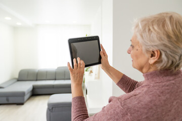 technology, automation and efficiency concept - smiling senior woman in glasses with tablet computer using smart home app over grey background