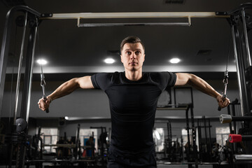 Fototapeta na wymiar Caucasian male athlete in the gym shakes the muscles of the arms and chest. The appearance of a handsome athlete during training.