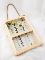 Fototapeta na wymiar Flower arrangement of dried flowers in narrow glass vases in a frame made of natural wood. Yellow, beige, green colors