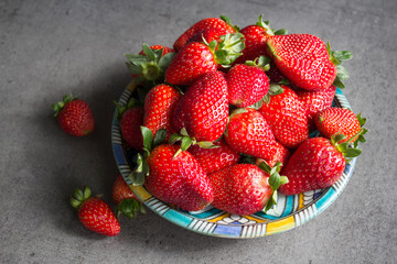 Juicy strawberries on blue ceramic plate. Fresh berries close up photo. Grey textured background. 