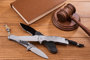 Few foldings knives, a judge s gavel and a book on wooden table