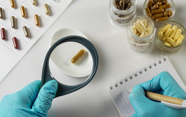 Hand of pharmacist holds a capsule with dietary supplements and magnifying glass