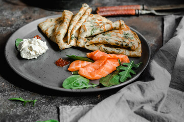 Thin pancakes with herbs, salmon and cream cheese on a plate. crepes