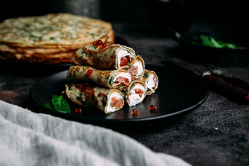 Thin pancakes with herbs, salmon and cream cheese on a plate. crepes