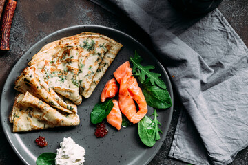 Thin pancakes with herbs, salmon and cream cheese on a plate. crepes