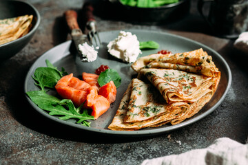 Thin pancakes with herbs, salmon and cream cheese on a plate. crepes