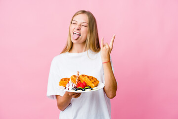 Young russian woman eating a waffle isolated showing rock gesture with fingers
