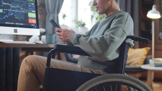 Midsection shot of disabled woman on wheelchair messaging on smartphone while having break during workday in home office