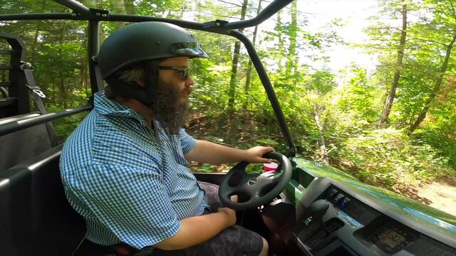 bearded man driving utv through forest and under fallen tree sunny pov passenger view