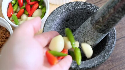 Slow motion of red chili pepper and garlic falling into the stone mortar to cook Spicy Shrimp Paste Chili Sauce, favorite Thai food (Nam Prik Ka Pi)