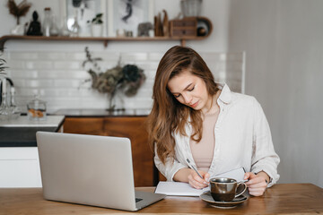 Smiling woman working with laptop drinking coffee, working at home, remote education