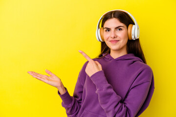 Young caucasian woman listening to music with headphones isolated on pink background excited holding a copy space on palm.