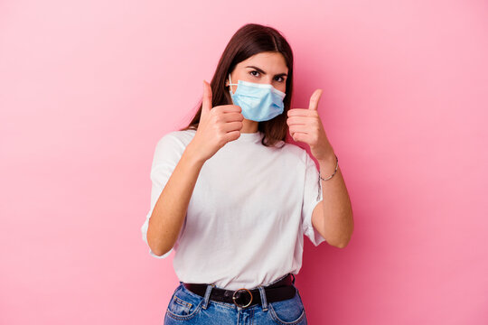 Young Caucasian Woman Wearing A Mask For Virus Isolated On Pink Background With Thumbs Ups, Cheers About Something, Support And Respect Concept.