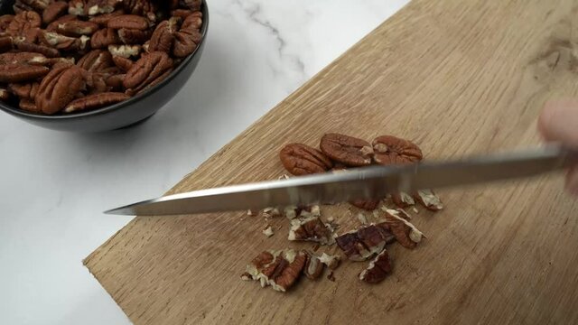 Pecans being chopped with large knife on wooden chopping board in slow motion. Pecan nuts food preparation concept.
