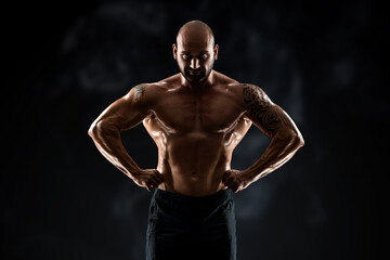 Fototapeta na wymiar Male bodybuilder with light stubble and bare torso shows muscularity against a dark background. The concept of a fitness club, doing sports, weightlifting. Copy space.
