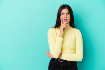 Young caucasian woman isolated on blue background looking sideways with doubtful and skeptical expression.