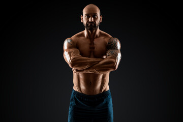 Fototapeta na wymiar Male bodybuilder with light stubble with a naked torso posing against a dark background. The concept of a fitness club, doing sports, weightlifting. Copy space.