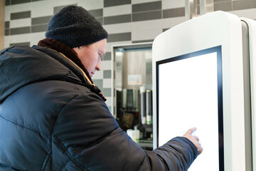 A man near self service restaurant, kiosk, terminal with empty screen