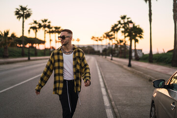 Chico joven guapo en mitad de carretera al atardecer con camisa amarilla