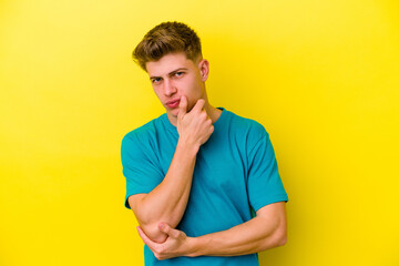 Young caucasian man isolated on yellow background suspicious, uncertain, examining you.