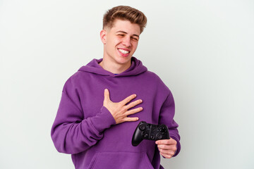 Young caucasian man holding a gamepad isolated on white background laughs out loudly keeping hand on chest.