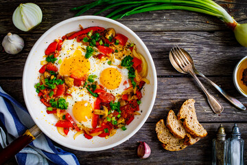 Shakshuka - fried eggs with sausages and vegetables in frying pan
