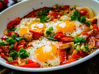 Shakshuka - fried eggs with sausages and vegetables in frying pan
