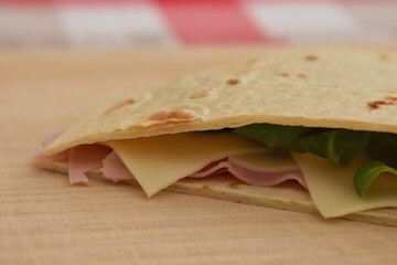 close up of Italian piadina romagnola with cheese, ham and salad, healthy food lifestyle, traditional