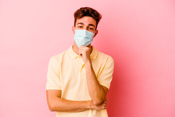 Young caucasian man wearing a protection for coronavirus isolated on pink background smiling happy and confident, touching chin with hand.