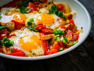 Shakshuka - fried eggs with sausages and vegetables in frying pan
