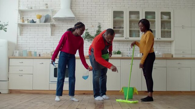 Strict handsome african american single father checking adorable teenage daughters mopping floor, making reprimand while united family making housekeeping with detergents during spring cleaning.