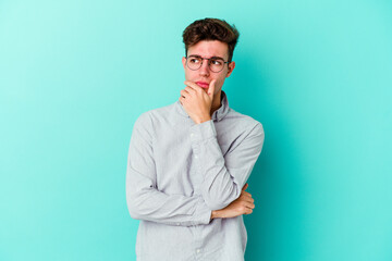 Young caucasian man isolated on blue background suspicious, uncertain, examining you.