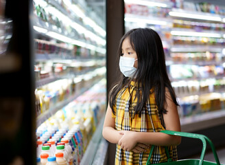 Asian child or kid girl wearing white face mask for close mouth nose and flu cough sick to protect coronavirus covid-19 or dust with holding basket for shopping milk in supermarket or department store