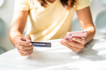 Young asian woman holding a credit card and using smart phone for make an online shopping payment at home