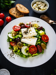 Fresh Greek salad - feta cheese, tomatoes, cucumber, lettuce, black olives and onion on wooden table
