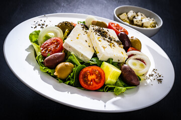 Fresh Greek salad - feta cheese, tomatoes, cucumber, lettuce, black olives and onion on wooden table
