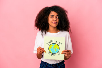 Young african american curly woman holding a planet message on a placard confused, feels doubtful and unsure.