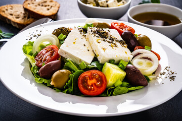 Fresh Greek salad - feta cheese, tomatoes, cucumber, lettuce, black olives and onion on wooden table
