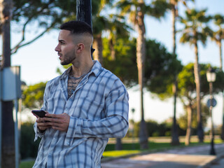 Hombre joven usando su teléfono móvil apoyado en una farola