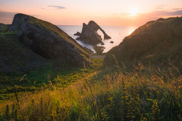 Sunrise or sunset golden light across a beatuful seascape of Bow Fiddle Rock sea arch on the rocky shore of Portknockie on the Moray Firth in Scotland.