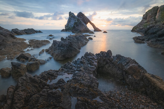 Beautiful dramatic sescape scenery at sunrise or sunset of Bow Fiddle Rock sea arch on the rocky shore of Portknockie on the Moray Firth in Scotland.
