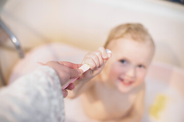 Mom gives baby kids toothbrush. girl is taking a bath. Hygiene procedures before going to bed. Toddler brushes teeth with a toothbrush.